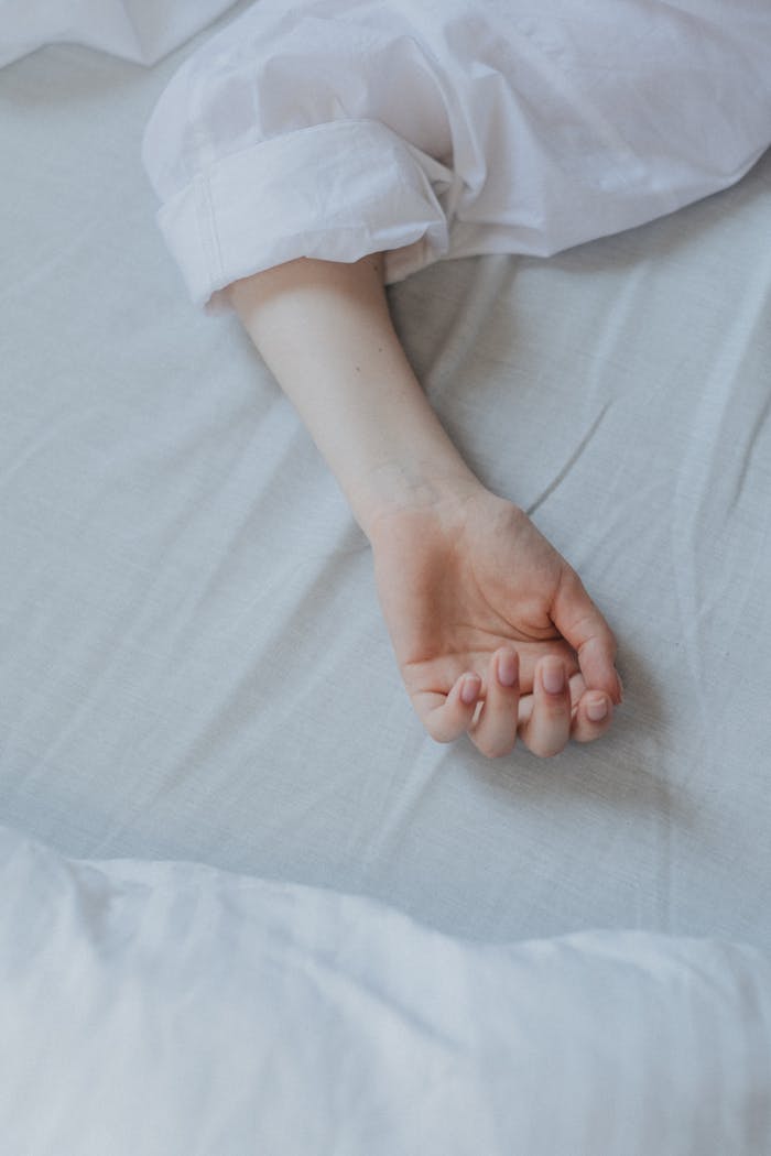 Close-up of a relaxed arm resting on a white bed sheet, suggesting tranquility.